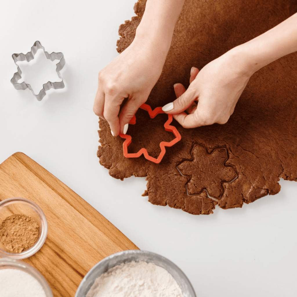 Woman using 3D snowflake cookie cutter to cut out cookies.